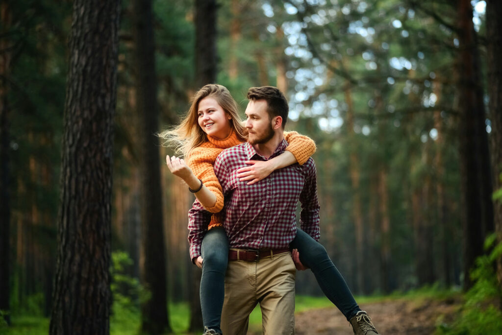 Iloinen pari ulkoilee metsässä, mies kantaa naista selässään.